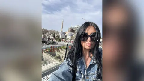 Stylish woman in denim jacket and sunglasses posing before the historic Hagia Sophia mosque under a cloudy sky.