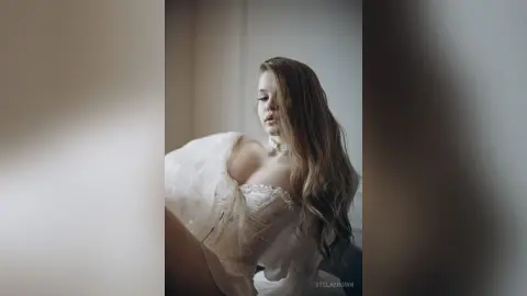 StelaBrown wears a white lace corset and long wavy hair while looking down.