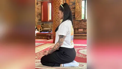 Young woman in white t-shirt meditating on a red rug in a traditional temple setting.