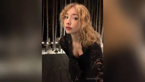 Blonde woman in a black lace top posing in a dark forest setting at night.