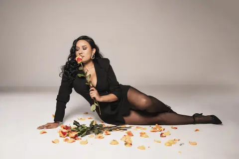 Elegant woman in a black dress sitting on a studio floor with scattered rose petals for a romantic mood.