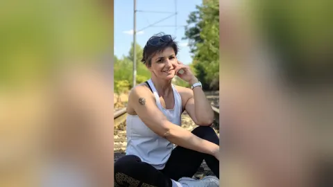 JaneHope — JaneHope sits on train tracks wearing a white tank top and black leggings.