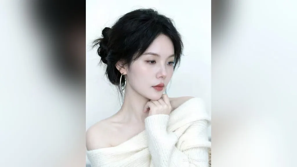 Young woman with short grey hair and silver hoop earrings posing against a white background.