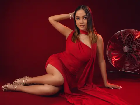 Elegant woman in a flowing red evening gown posing gracefully against a deep red studio background.
