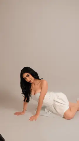 Smiling woman in a white strapless dress posing on a neutral studio background.