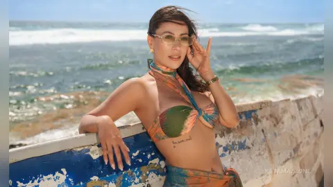 Smiling woman in colorful patterned bikini relaxing by the ocean waves on a sunny beach day.