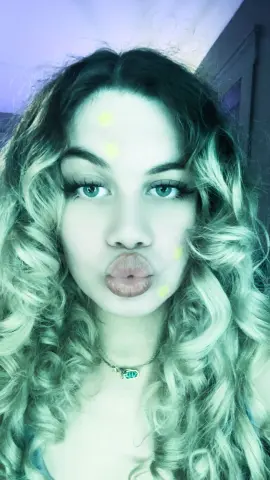 Young woman with curly blonde hair and blue eyes making a pouty face in a soft teal aesthetic filter.