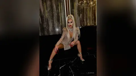 Glamorous woman in a sparkling silver sequin dress posing in a luxury dark lounge setting.