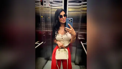 Stylish woman in a white lace crop top and red trousers taking a mirror selfie in an elevator.
