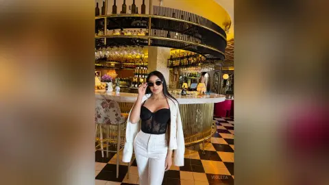 Stylish woman in a white blazer and black lace corset posing in a luxury modern bar with checkered floors.