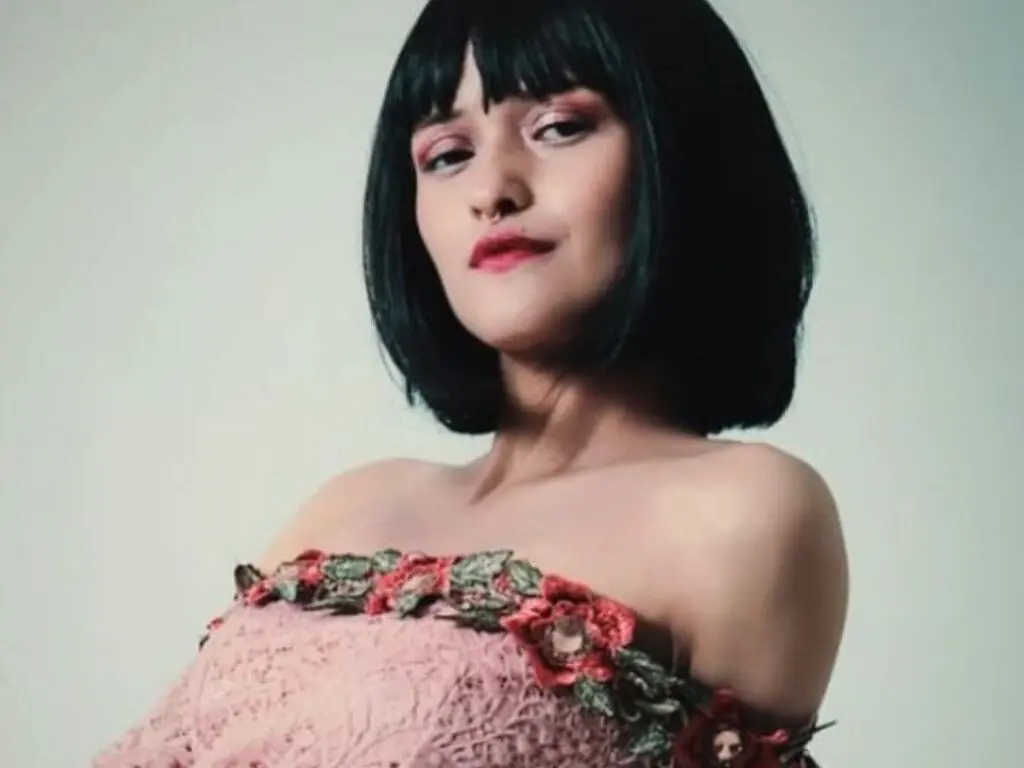 Portrait of a woman with black bangs wearing a pink floral lace strapless dress in a soft studio setting.