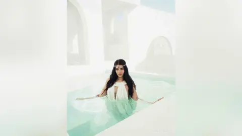 Mystical woman in a white flowing dress relaxing in a bright, ethereal turquoise pool setting.