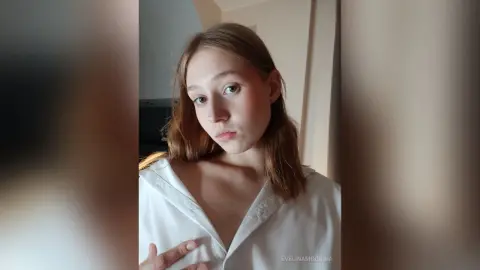 Young woman in a white silk shirt posing with a soft, natural look in a bright indoor setting.