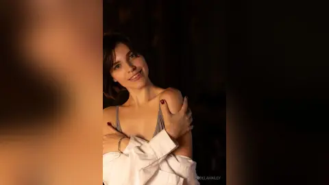 Smiling young woman in a white shirt relaxing in warm, moody indoor lighting.