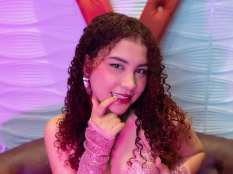LuciiaBeltran — Smiling young woman with curly hair wearing a pink sequin outfit in a dreamy pastel lit room.