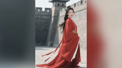 Elegant woman in a flowing red traditional Hanfu dress standing by the historic Great Wall of China.