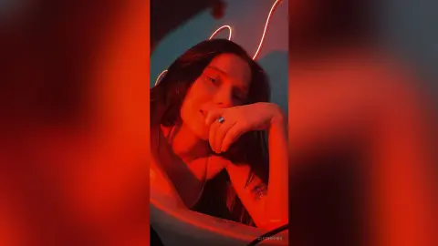 Young woman in a white top posing under moody red neon lights for a cinematic aesthetic portrait.