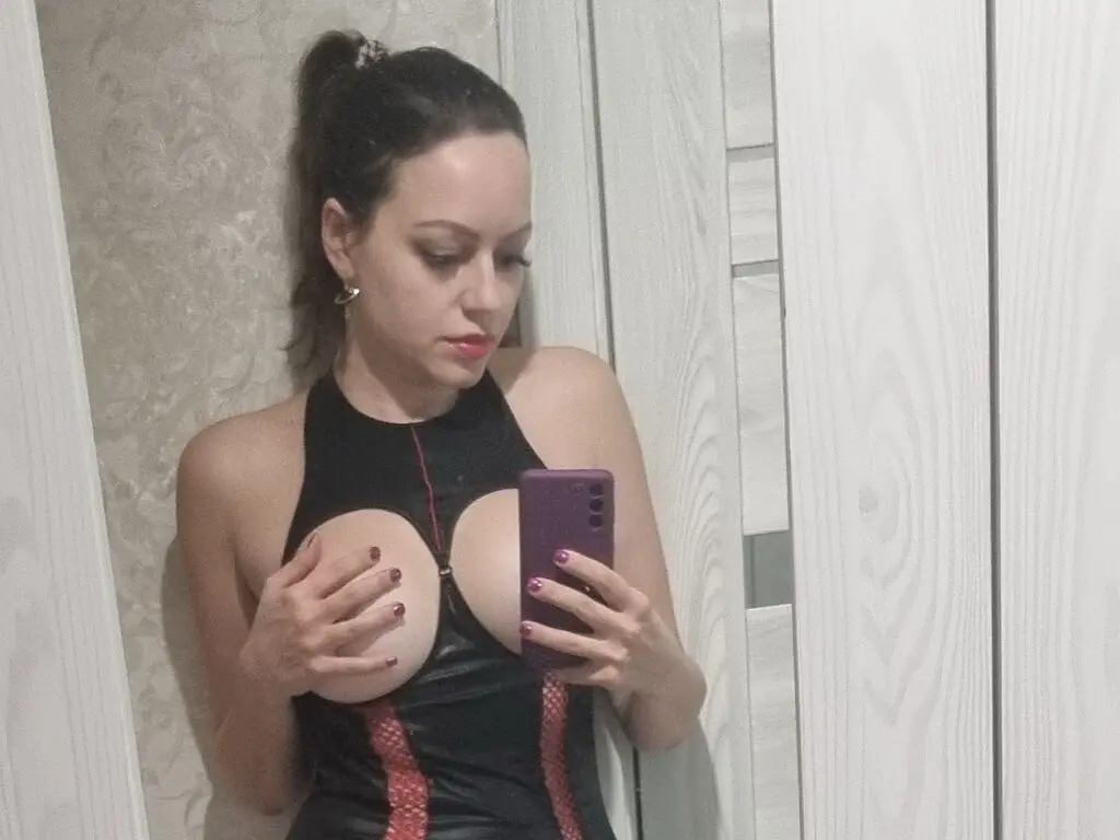 Young woman in a black sleeveless bodysuit posing for a mirror selfie in a modern room.