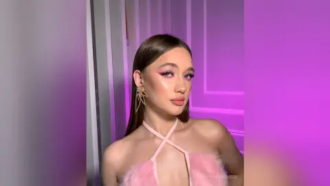 StephanieRiggi poses in a pink halter top with her hair slicked back and sparkly eye makeup.