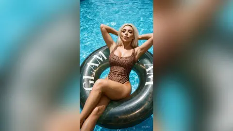 Blonde woman in a brown textured swimsuit relaxing on a black inflatable ring in a bright blue swimming pool.