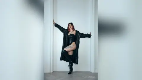 Edgy woman in black leather bodysuit and tall boots posing confidently in a minimalist white studio.