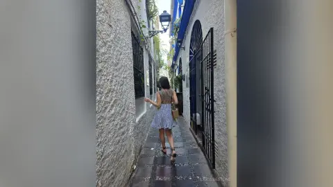 Woman in a floral summer dress walking through a narrow, charming European cobblestone alleyway.