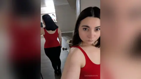 SashaMaroon wears a red tank top and black leggings while standing in a room.