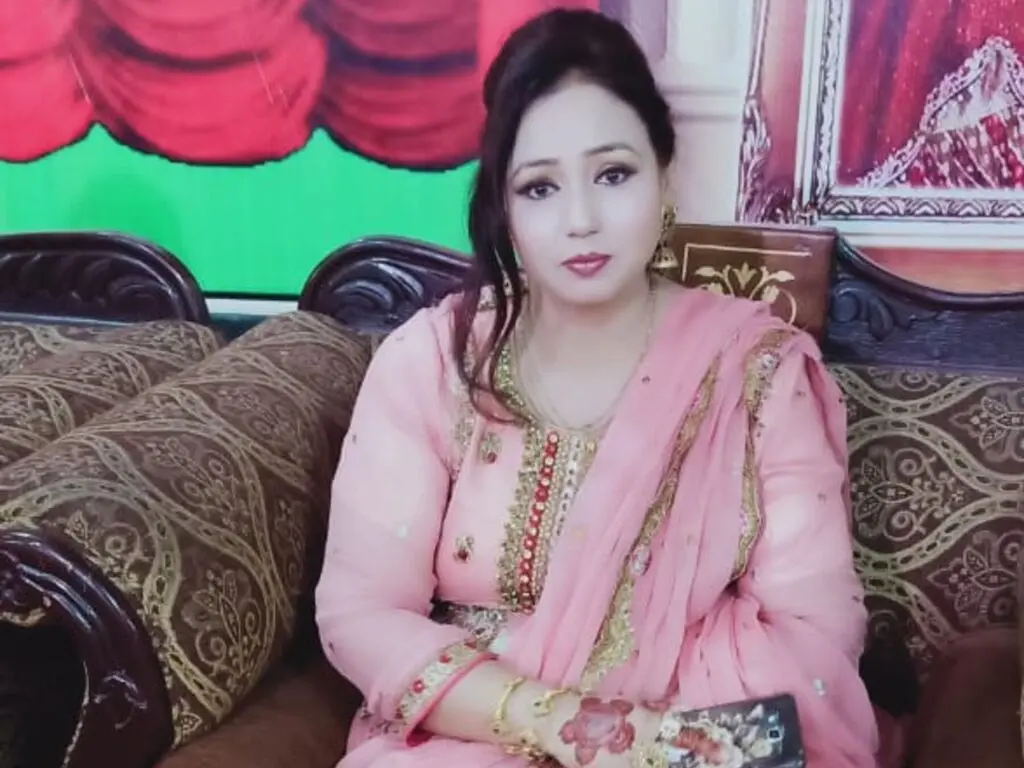 Woman in elegant pink traditional Indian salwar kameez sitting on a patterned sofa in a festive setting.