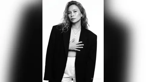 MilaSwan — MilaSwan poses in a black blazer and white shorts with her hand on her chest against a white background.