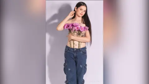 Young woman in denim jeans holding a pink flower bouquet against a white background for a dreamy portrait.