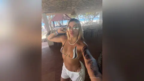 Blonde woman in a striped bikini and white shorts relaxing at a tropical beachside cafe.