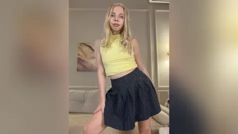 Blonde woman in a yellow halter top and navy pinstripe skirt posing in a bright modern living room.