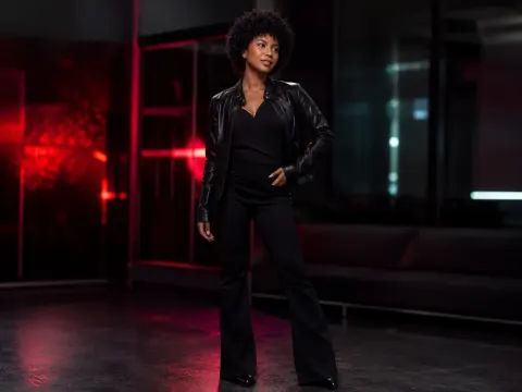KylieDecks — KylieDecks stands in a dark room wearing a black leather jacket and black pants.
