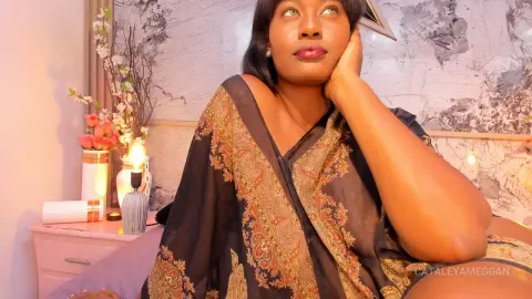 Thoughtful Black woman in a patterned brown kaftan relaxing in a cozy, warm-lit bedroom setting.