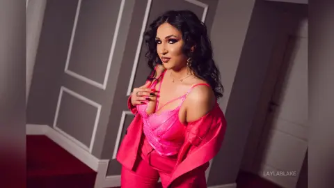 Glamorous woman in a pink lace bodysuit and blazer posing in a modern indoor setting with a confident mood.