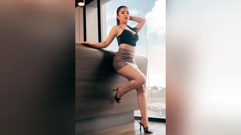 VickyPortman poses leaning against a wooden counter wearing a black bra and a short brown skirt.