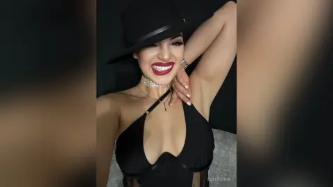 Smiling woman in a black halter top and wide-brimmed hat posing against a dark studio background.