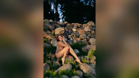 Fashionable woman in a beige bodysuit sitting on a rocky mountain landscape during a golden hour sunset.