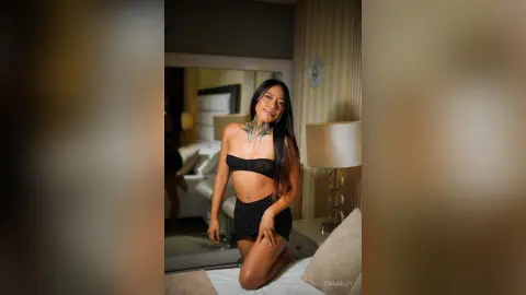 EmaWildy poses kneeling on a bed wearing a black lace bra and matching panties.