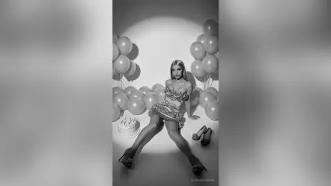 Glamorous woman in a sequined mini dress posing with balloons in a dreamy black and white studio setting.