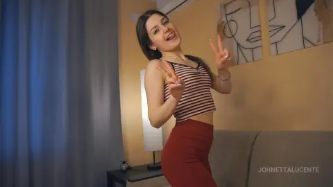 Cheerful young woman in a striped crop top and red skirt making peace signs in a cozy living room.