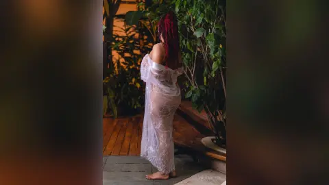 Woman in a sheer white lace gown standing in a lush tropical garden at night.