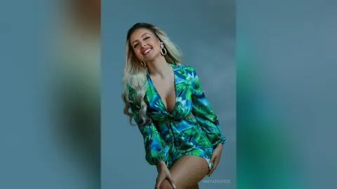 Anita smiles while wearing a low-cut green tropical print dress that shows cleavage.