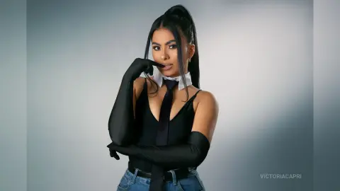 Elegant woman in a black bodysuit, tie, and long gloves posing against a studio background.