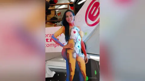 Smiling woman in colorful body paint art standing in a bright indoor studio setting.