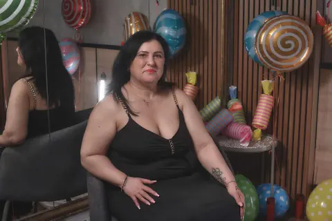 Curvy woman in a black slip dress sitting by colorful party balloons in a modern room.