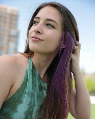Smiling young woman with long purple hair wearing a green halter top in a bright outdoor setting.