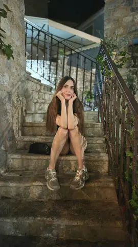 Young woman in casual shorts and sneakers sitting on stone stairs in a rustic outdoor setting.
