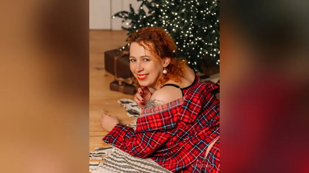 Redheaded woman in red satin lingerie and gloves lounging on a grey sofa with a glamorous mood.