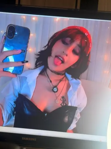 Young woman in a black corset and white shirt taking a playful selfie with a red headband and choker.